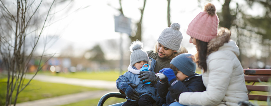 A young family sit on a bench in the park with winter hats on