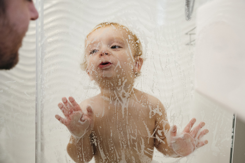A young boy kissing a shower screen which is covered in bubbles