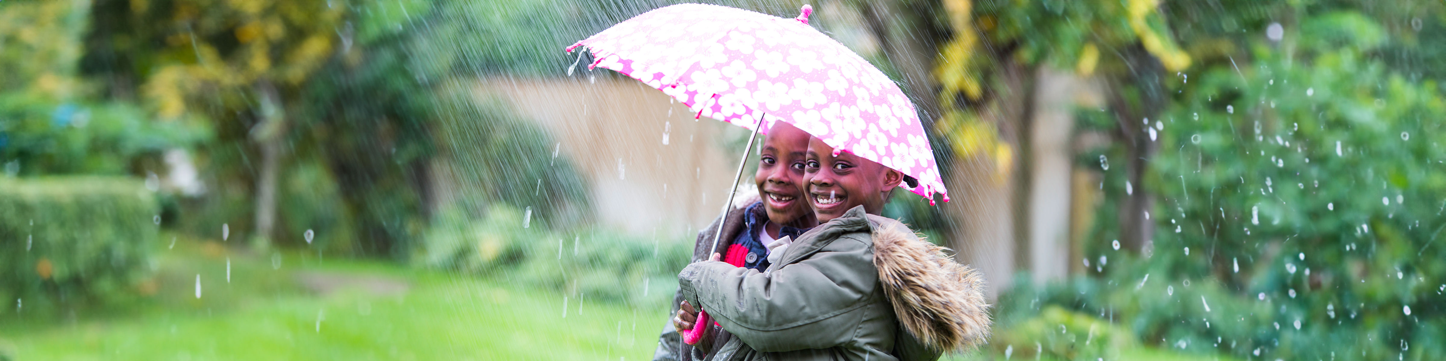 Two smiling young boys shelter under an umbrella from the rain