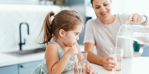 Woman pouring water into a glass with a child drinking water through a straw