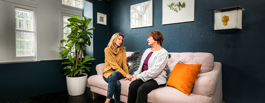 A mother and daughter sit on a sofa holding hands