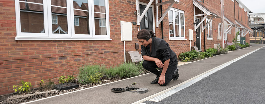 A person reads a water meter in the street outside their house