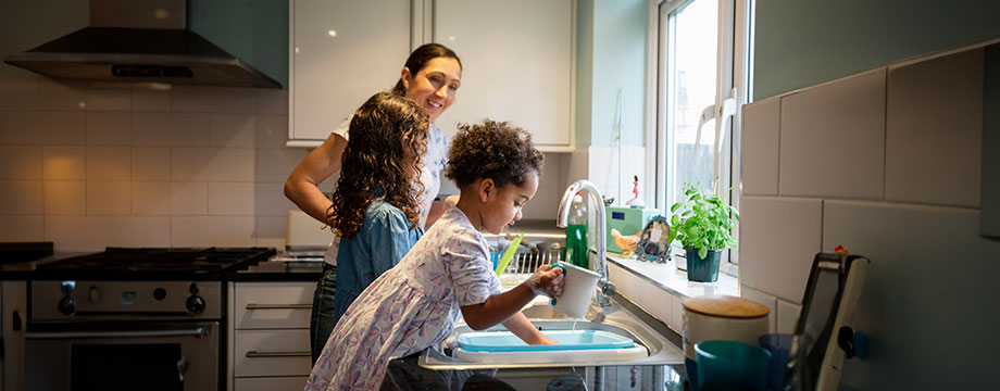 A child washes up dishes in the sink with her mother