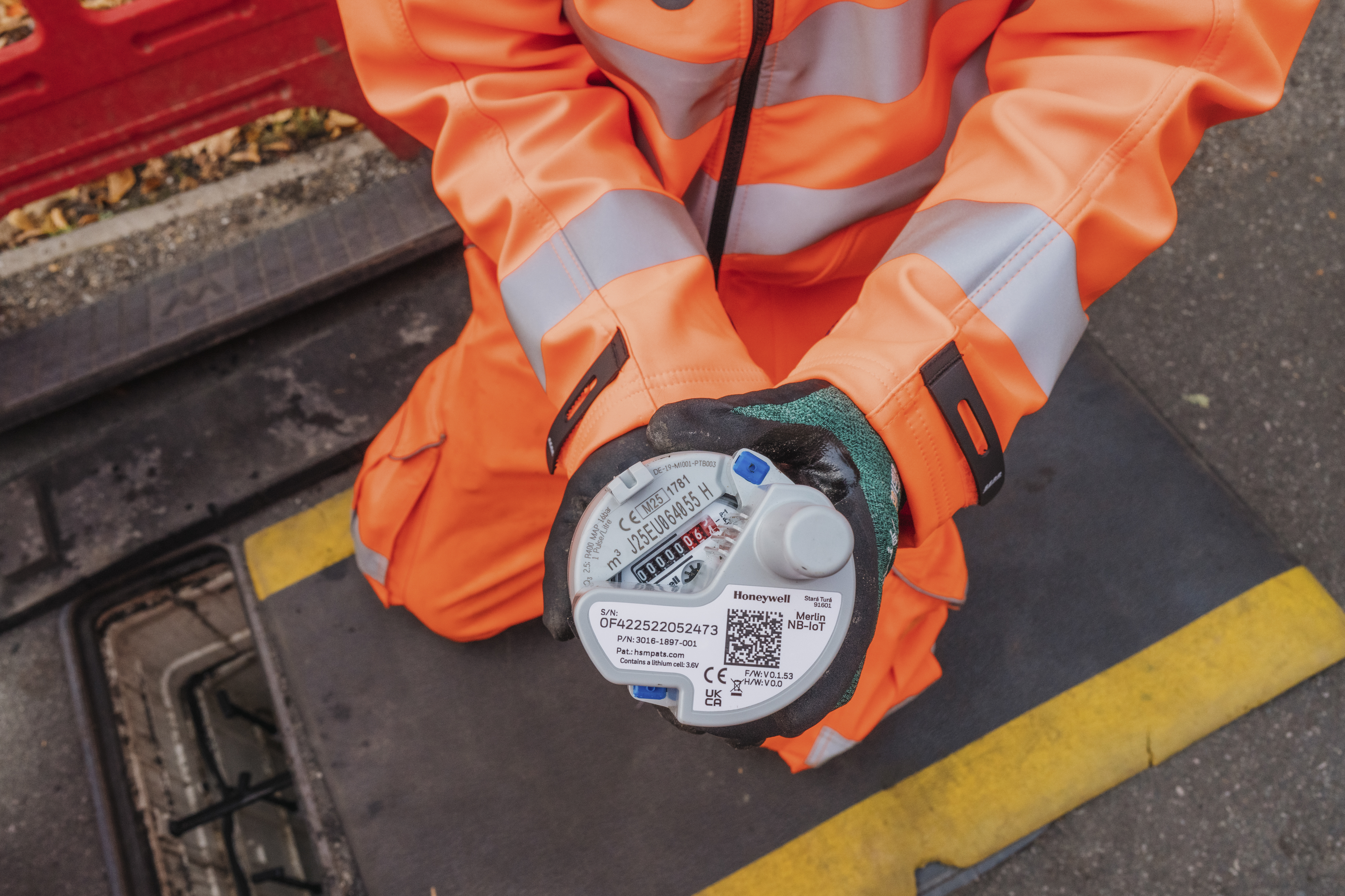 An engineer wearing orange high-vis clothing holds a smart meter
