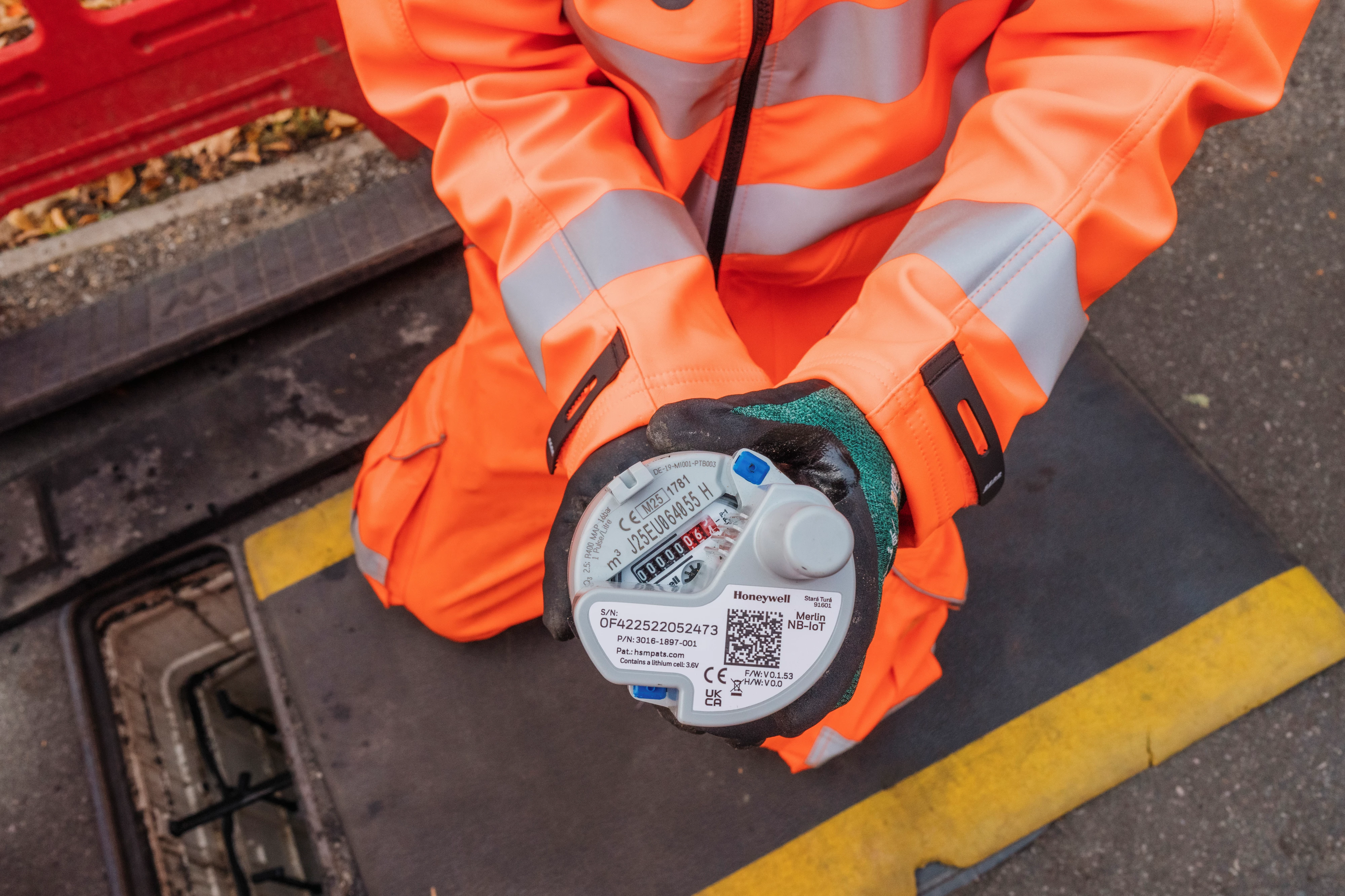 An engineer wearing orange high-vis clothing holds a smart meter