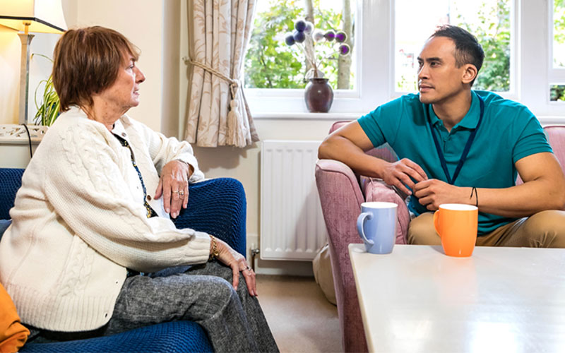 A man and woman sit down with cups of tea