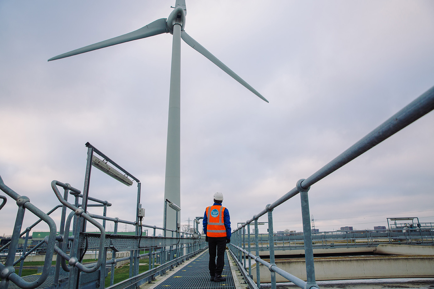 A man in orange high-vis looks at a wind turbine.