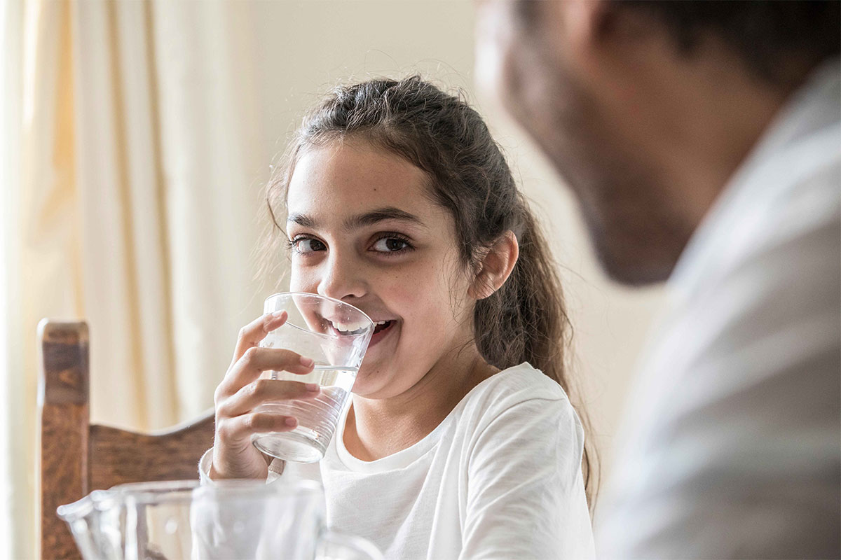 A young lady smiling while drinking a glass of water