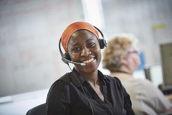 a lady in an orange headscarf wearing a headset smiling towards the camera