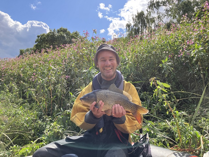 A man in a yellow waterproof holds a fish.