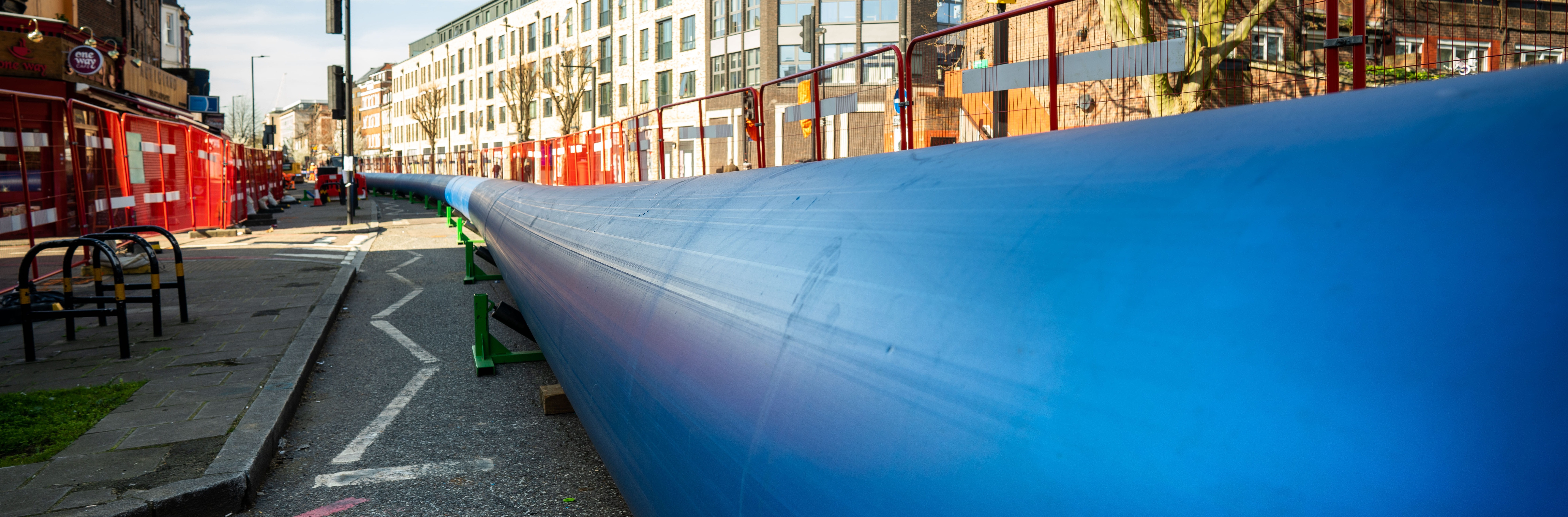 A large blue pipe sitting on a road behind barriers waiting to be installed under the road