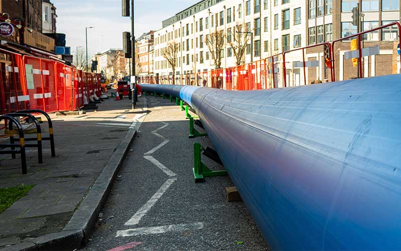 A large blue pipe sitting on a road behind barriers waiting to be installed under the road