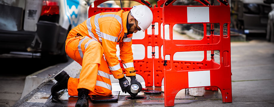 A workman holding a meter on the street pavement