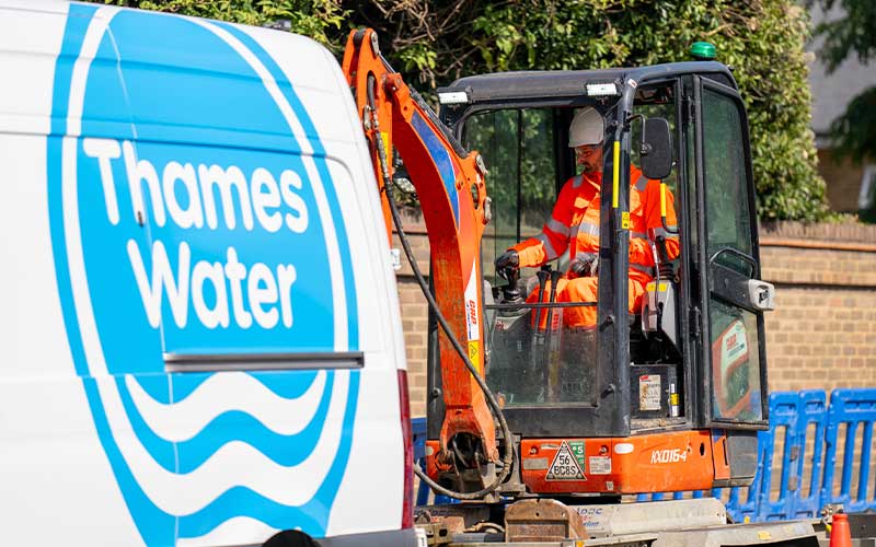 A repair team member operating a mini excavator behind a Thames Water van