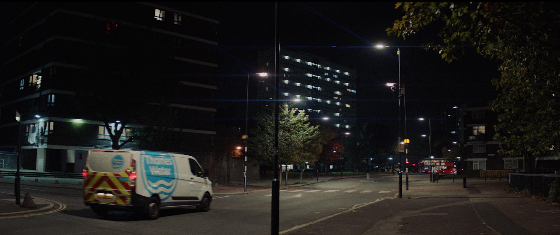 A white and blue Thames Water van drives down a residential street at night